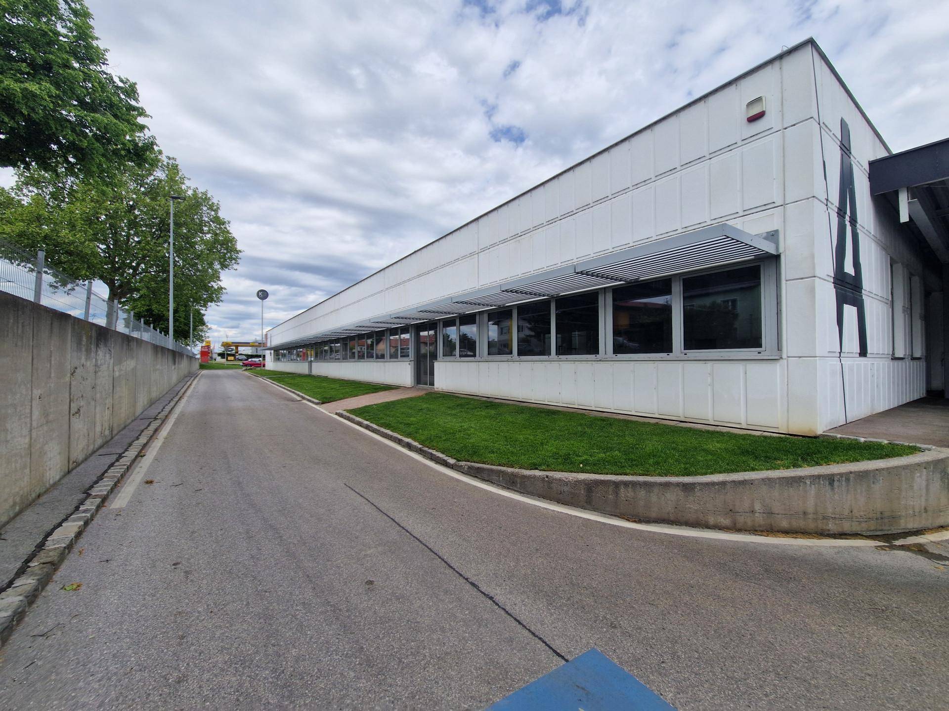 Langes, modernes Geschäftsgebäude mit großen Fenstern und Vordächern unter bewölktem Himmel und Grünflächen.
