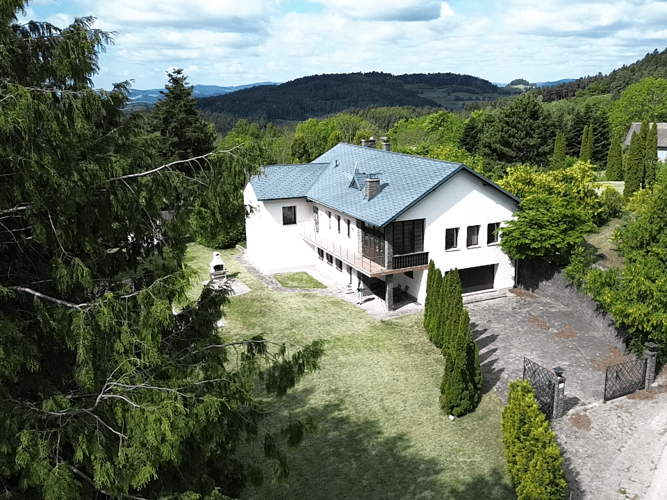 Ansicht des Haupthauses mit Balkon, gepflegtem Garten und weitem Blick auf die hügelige Landschaft.