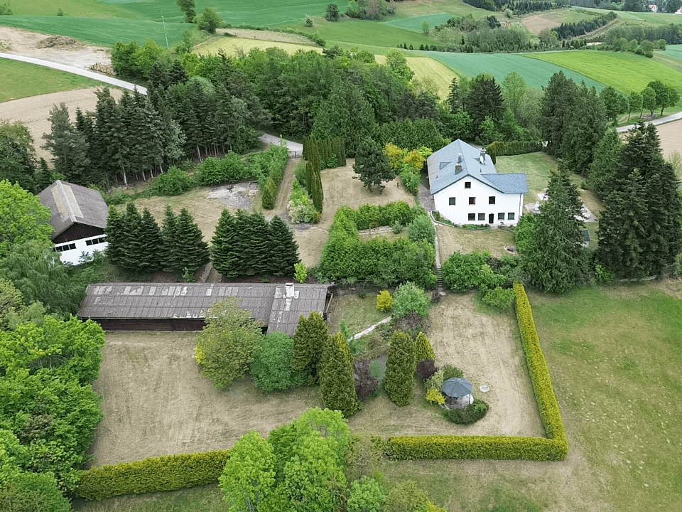 Luftaufnahme des Anwesens mit mehreren Gebäuden, weitläufigen Grünflächen und umgebender Natur.