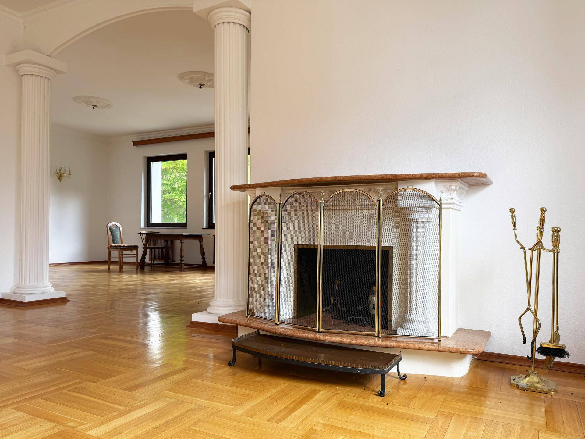 Elegantes Wohnzimmer mit klassischem Kamin, Säulen und Fischgrätparkettboden, hell und geräumig.