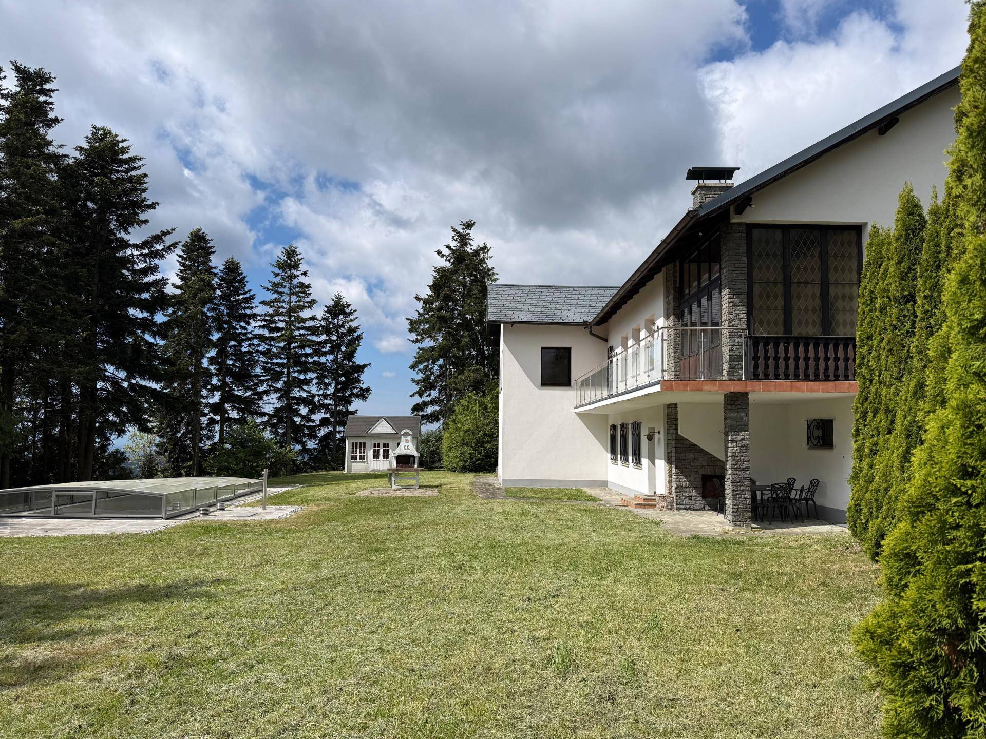 Seitenansicht des Haupthauses mit weitläufiger Rasenfläche, Grillplatz und einem Gartenhaus im Hintergrund.