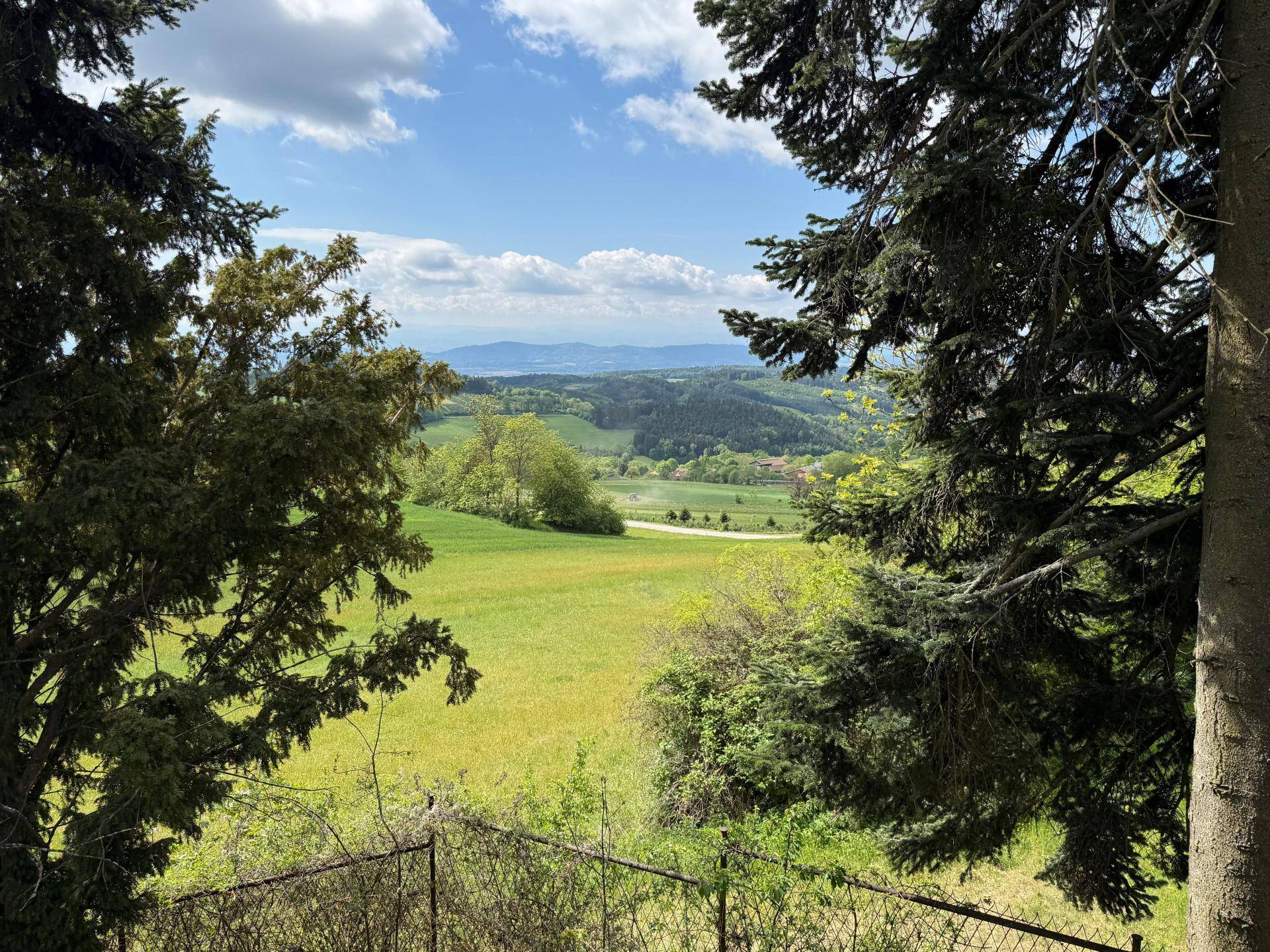 Malerischer Ausblick auf die weite grüne Landschaft und ferne Hügel unter blauem Himmel.