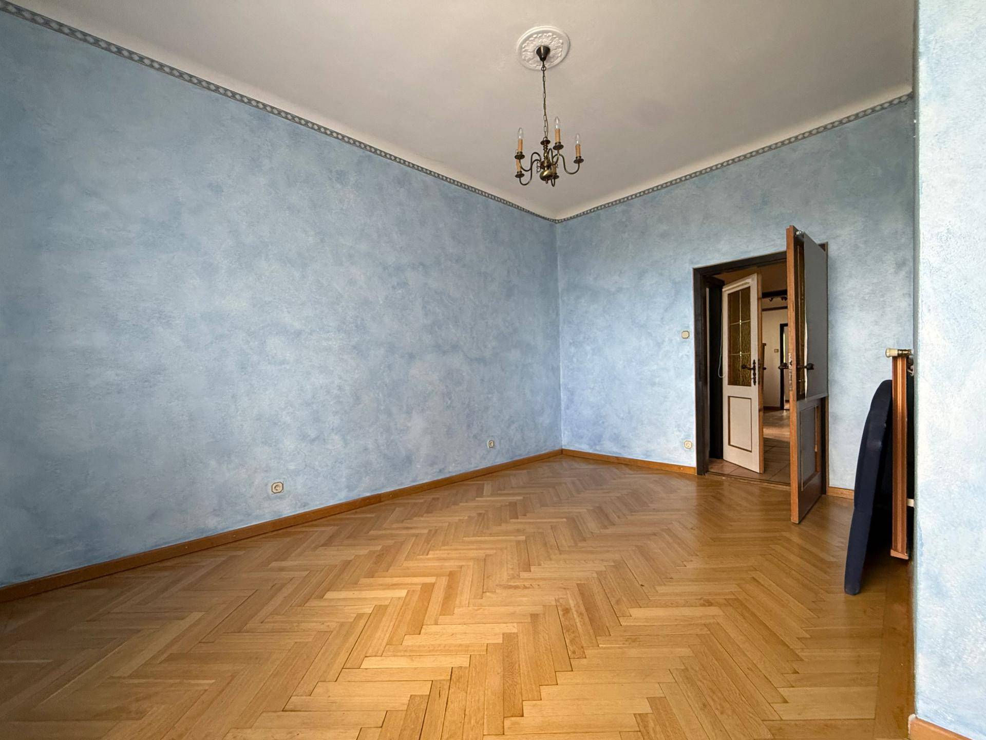Geräumiges Zimmer mit Fischgrätparkett, blauen Wänden und einem Kronleuchter an der Decke.