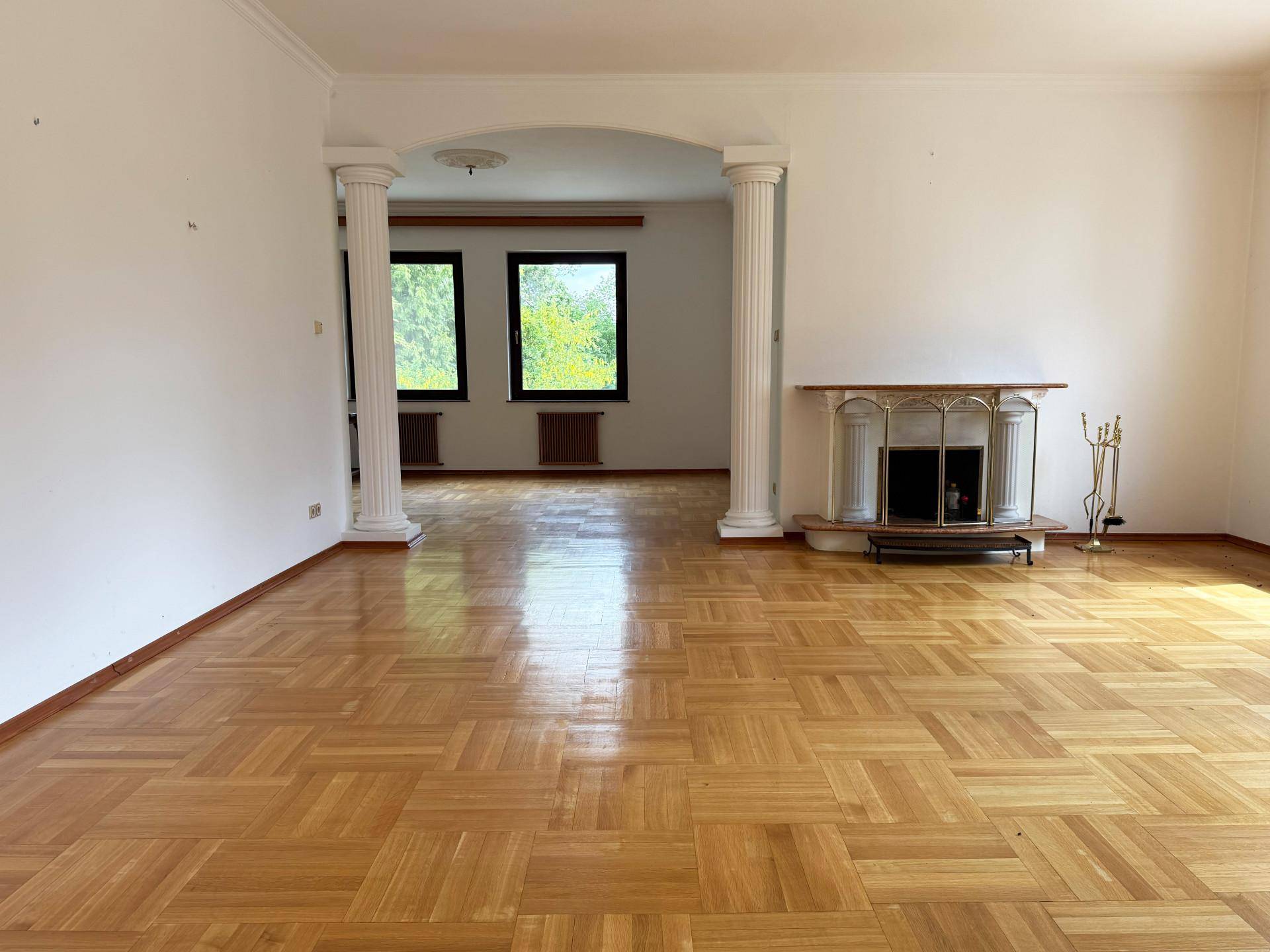 Geräumiges Wohnzimmer mit Parkettboden, dekorativem Kamin und Säulen, die den Raum gliedern.