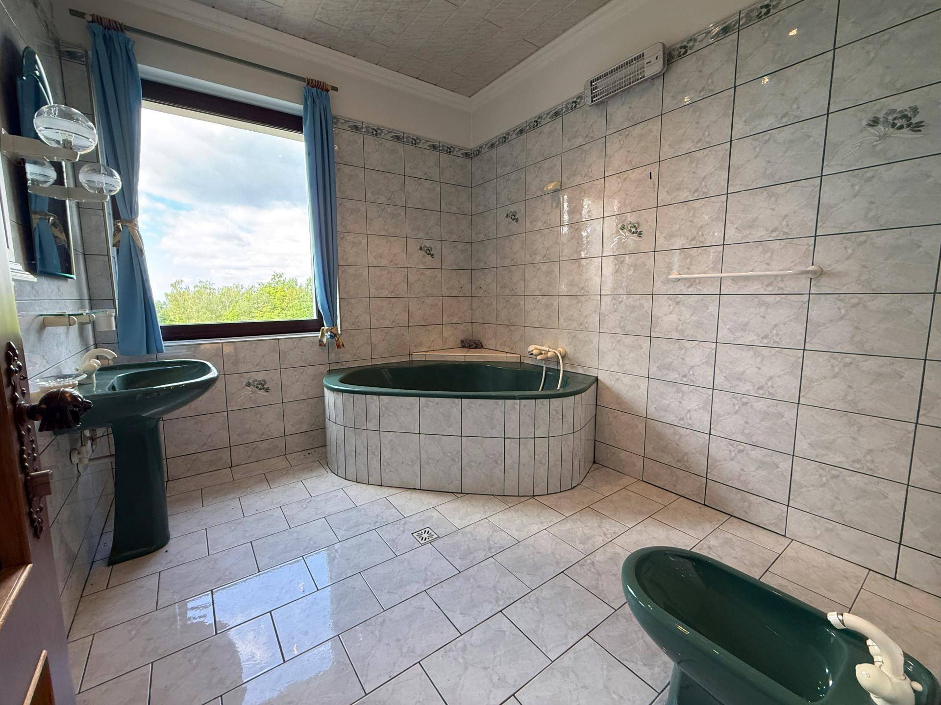 Badezimmer mit grünen Sanitäranlagen, weißen Fliesen und einer Badewanne unter dem Fenster.