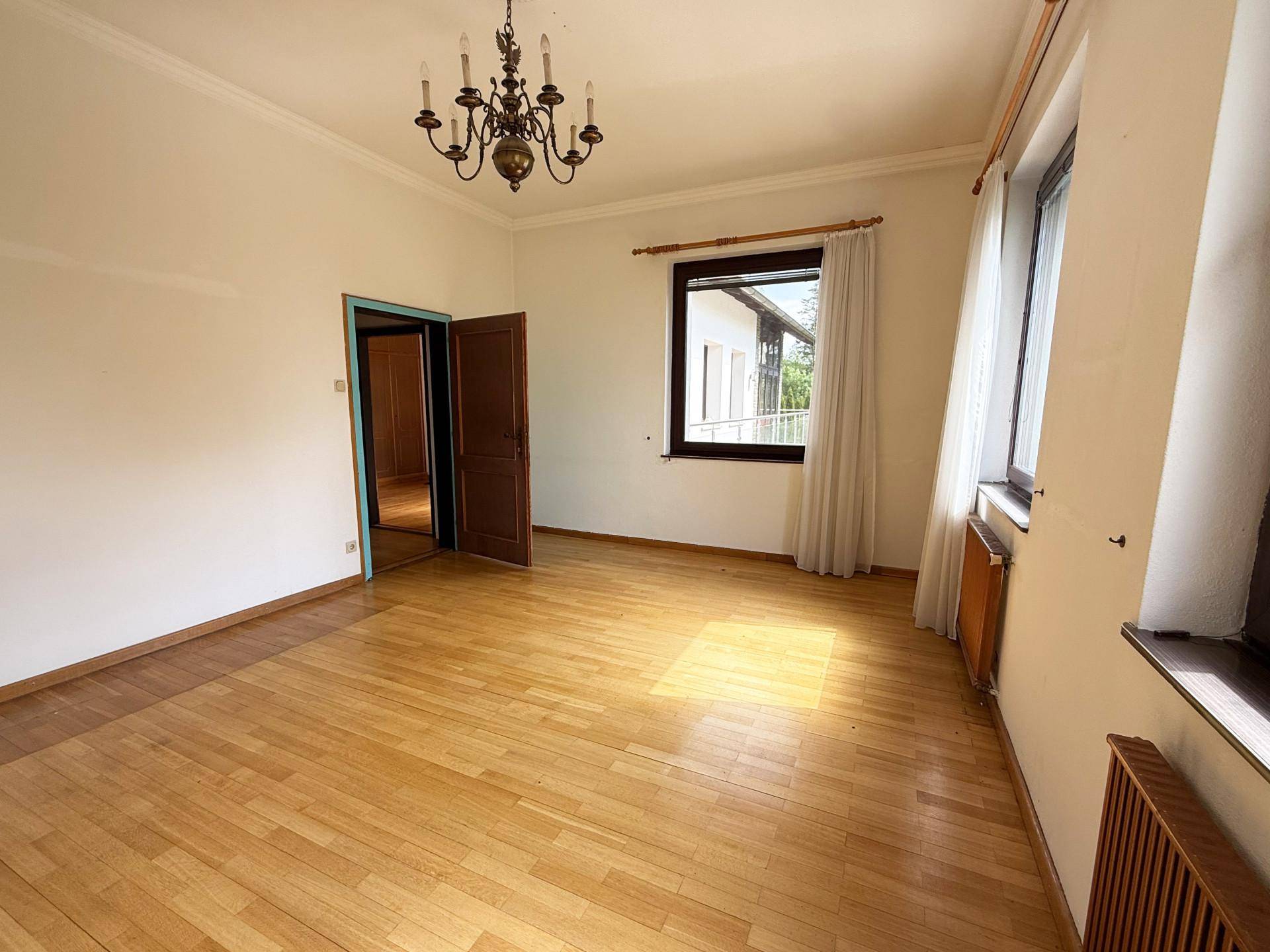 Helles Zimmer mit Holzparkettboden, weißen Wänden und zwei Fenstern, die viel Licht hereinlassen.