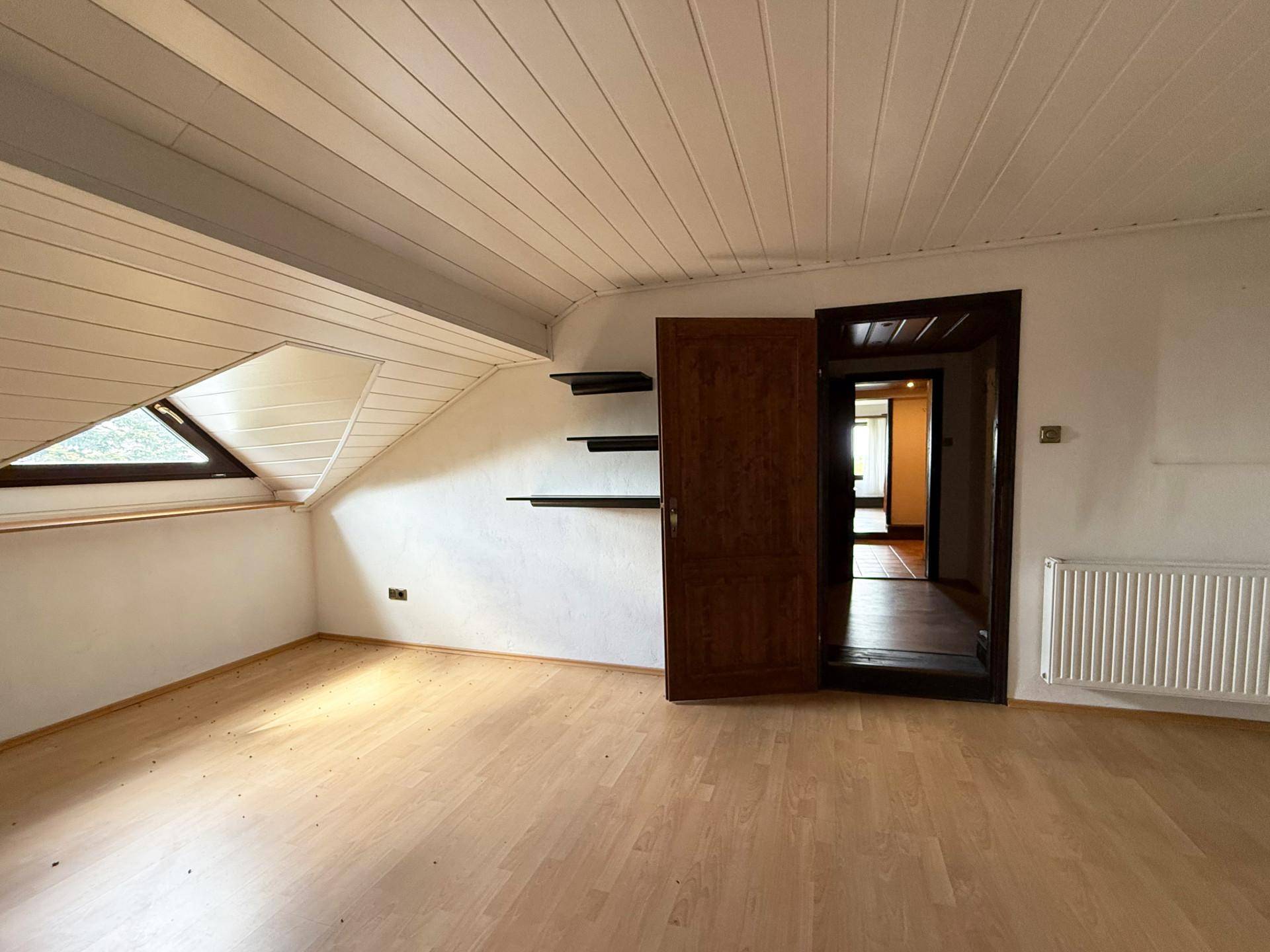 Helles Dachzimmer mit Holzpaneeldecke, Laminatboden und einem Dachfenster.