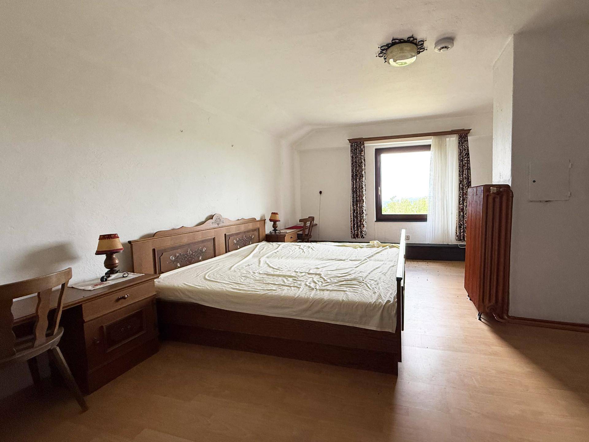 Schlafzimmer mit großem Holzbett, Laminatboden und einem Fenster, das viel Tageslicht hereinlässt.