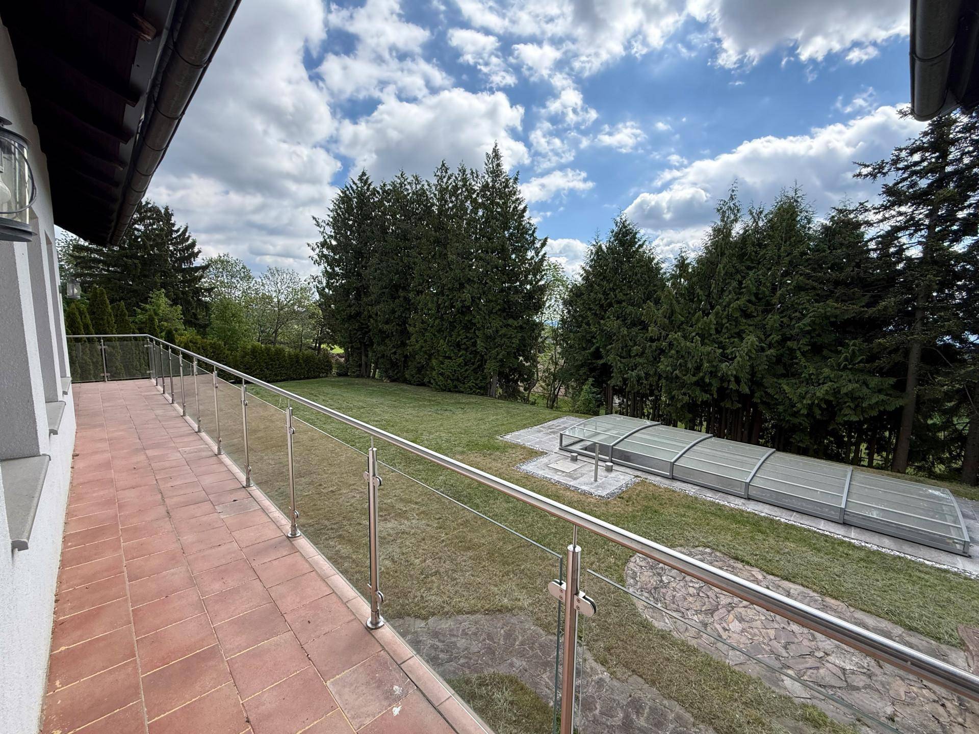 Große Terrasse mit Fliesenboden und Glasgeländer, bietet Blick auf den Garten und eine Poolabdeckung.