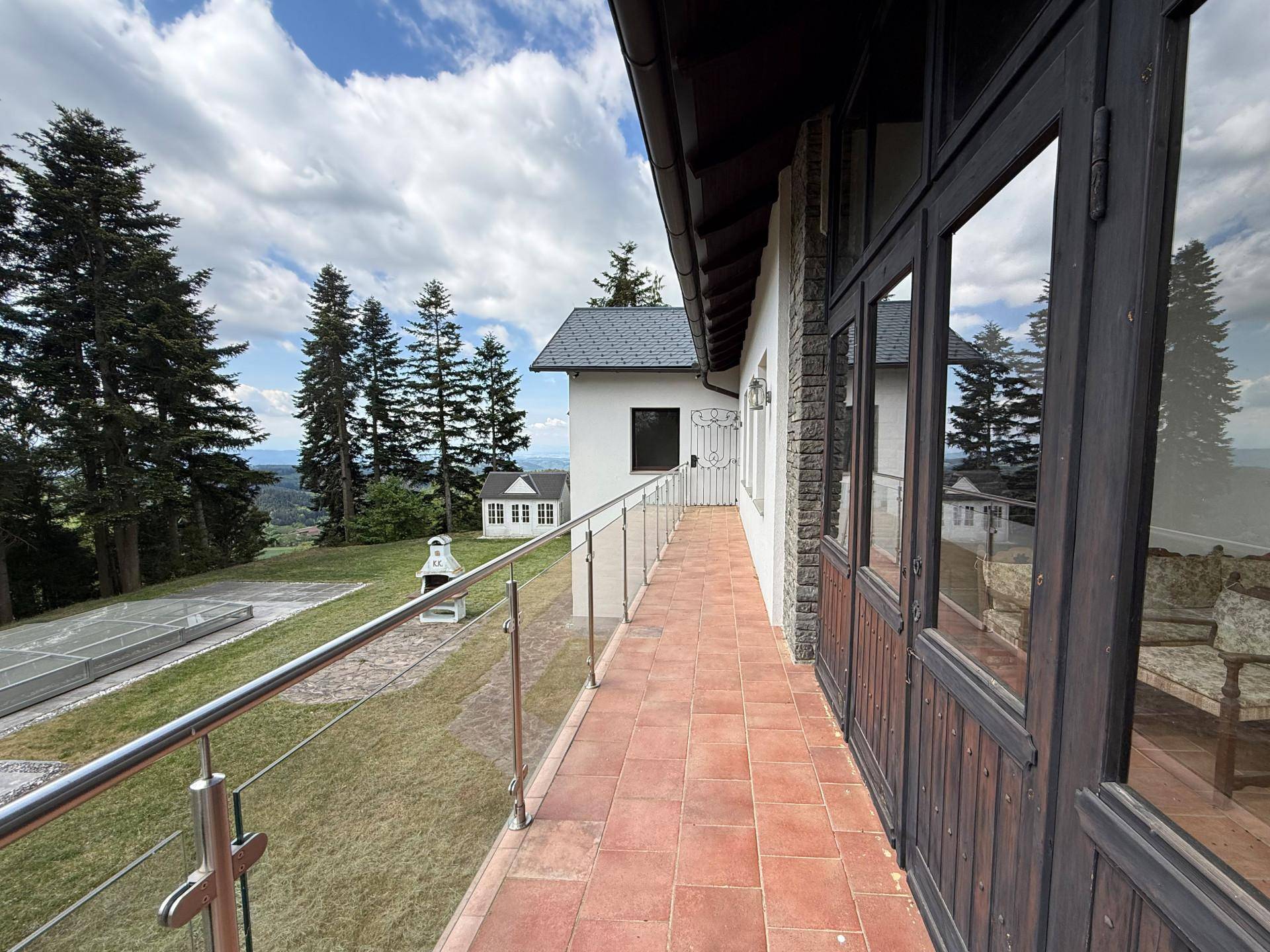 Langer Balkon mit Terracotta-Fliesen, Glasgeländer und weitem Blick über die grüne Landschaft.