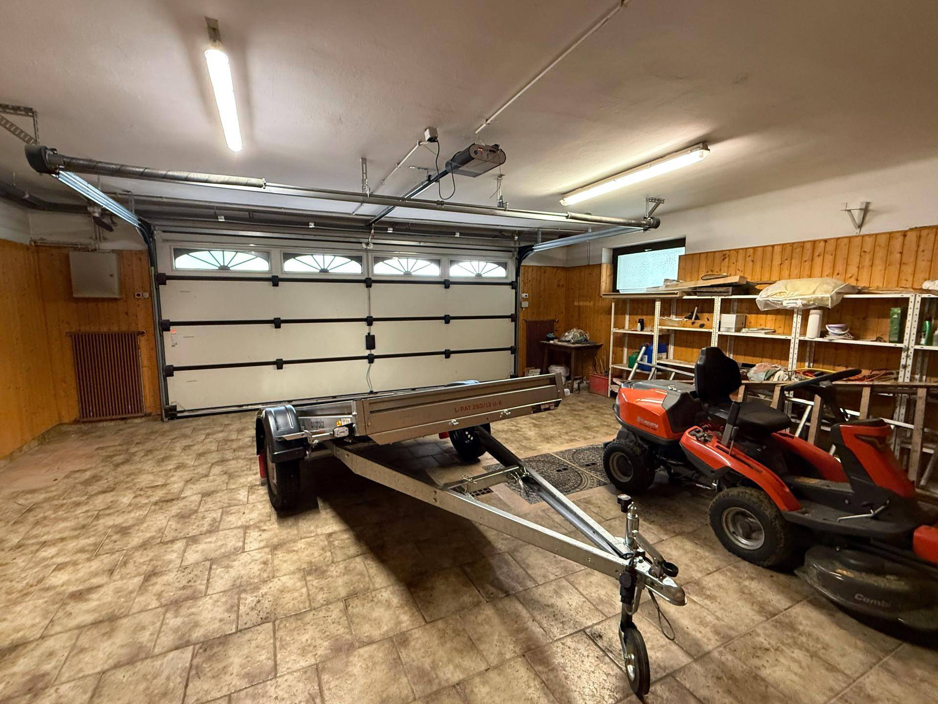 Geräumige Garage mit Fliesenboden, Rolltor und Stauraum für Fahrzeuge und Geräte.