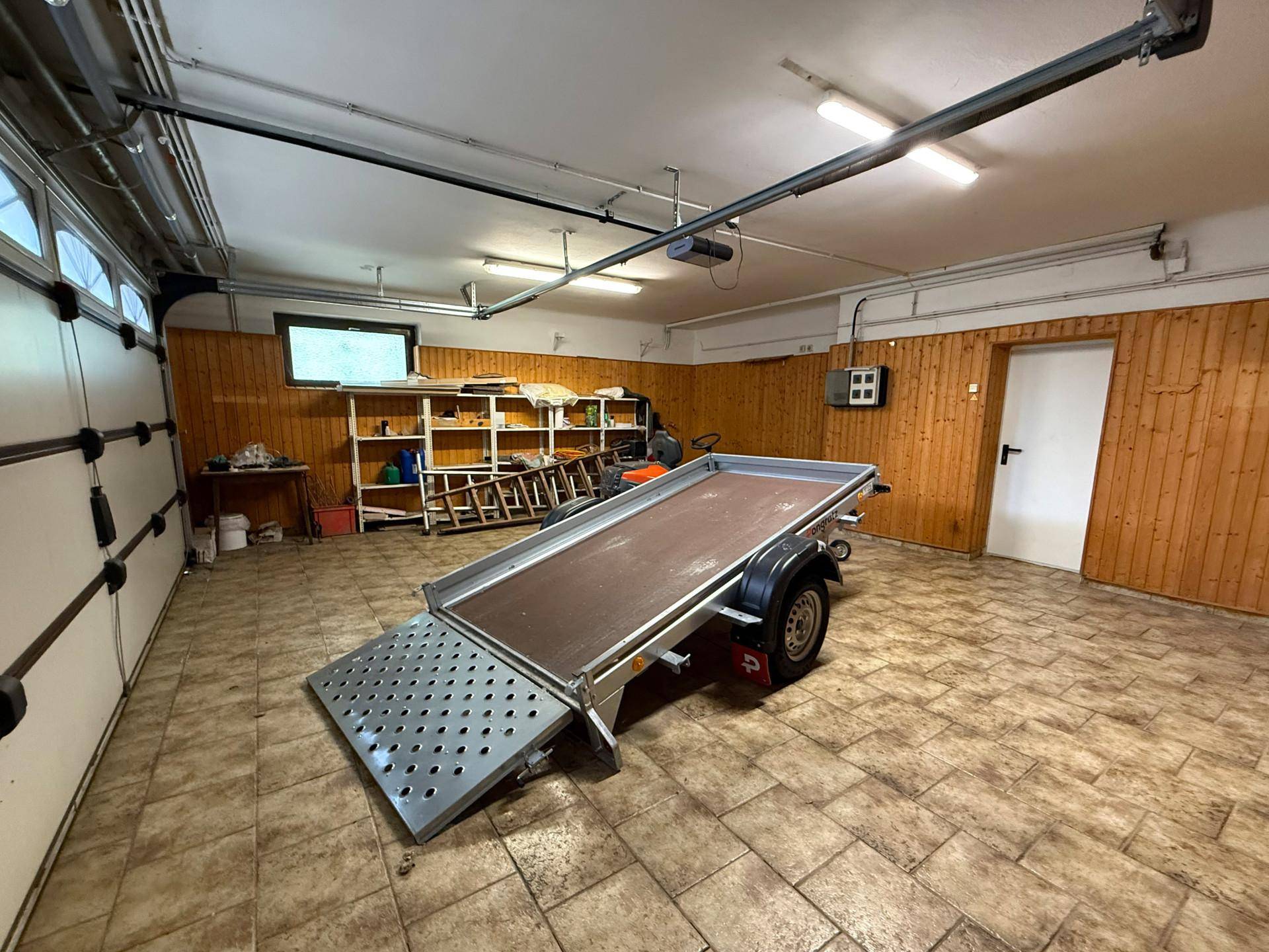 Innenansicht der Garage mit Holzwänden, Fliesenboden und einem Anhänger mit Rampe.