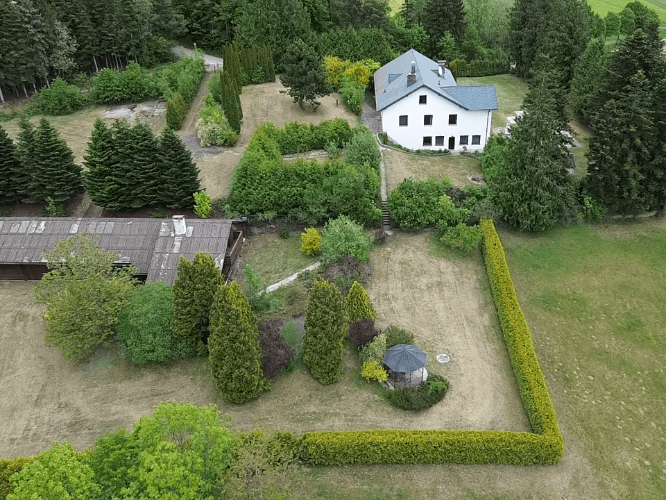 Luftaufnahme des weitläufigen Grundstücks mit Wohnhaus, Nebengebäude und gepflegten Hecken.