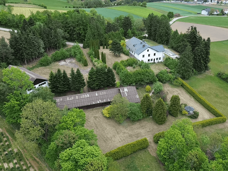 Luftaufnahme des weitläufigen Grundstücks mit Wohnhaus, Nebengebäude und umgebender Natur.