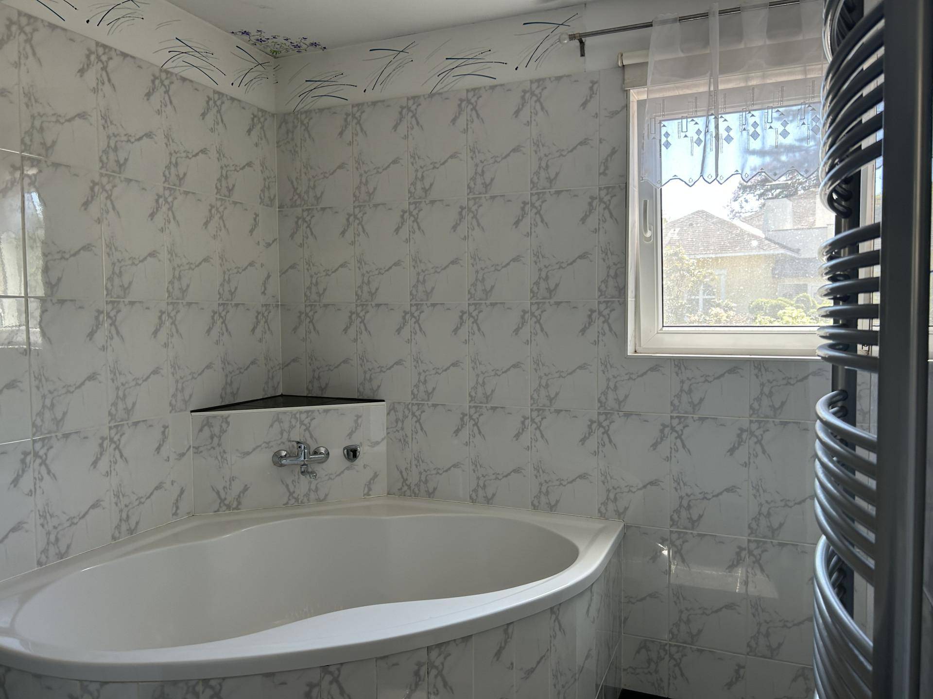 Helles Badezimmer mit Eckbadewanne, Fliesen und beheiztem Handtuchhalter.