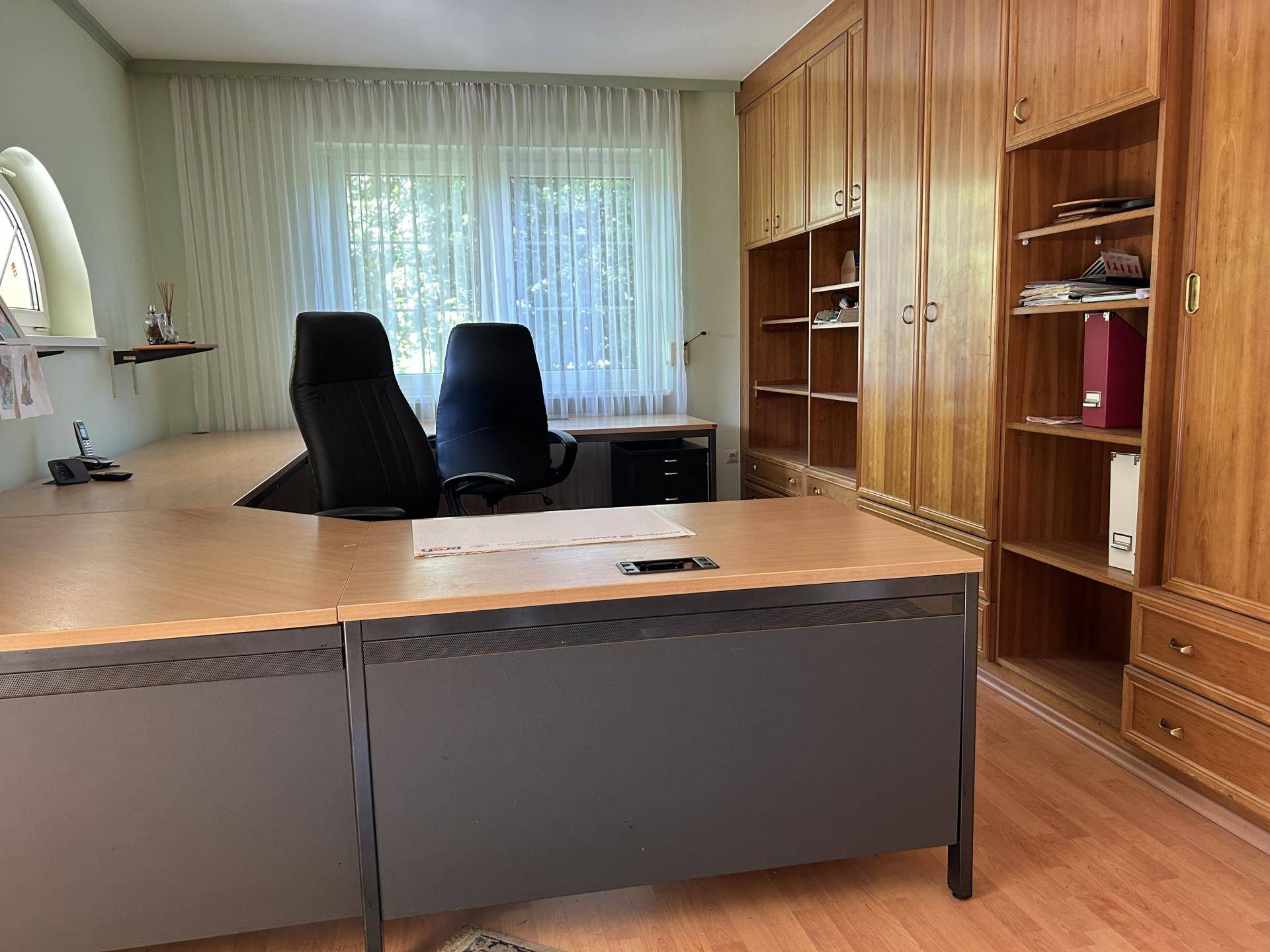Großes Büro mit Holzschränken, Schreibtisch und Blick ins Grüne.