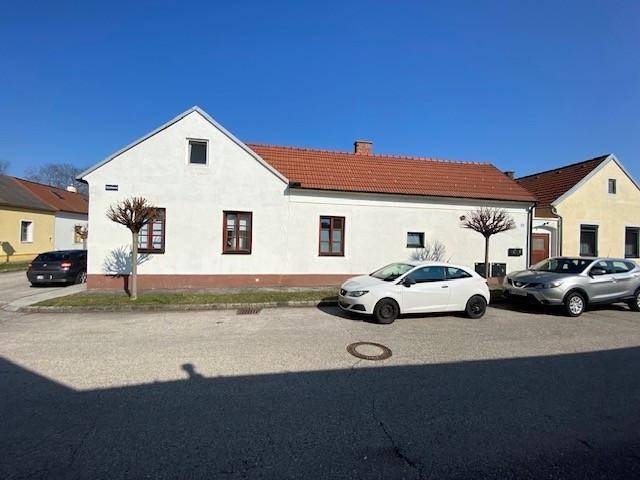 Weißes Einfamilienhaus mit rotem Ziegeldach und gepflegter Fassade an einer ruhigen Straße.