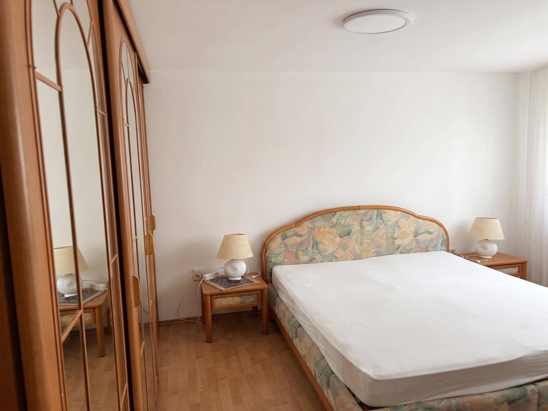 Schlafzimmer mit floral gemustertem Bett, Holzschrank und Parkettboden.
