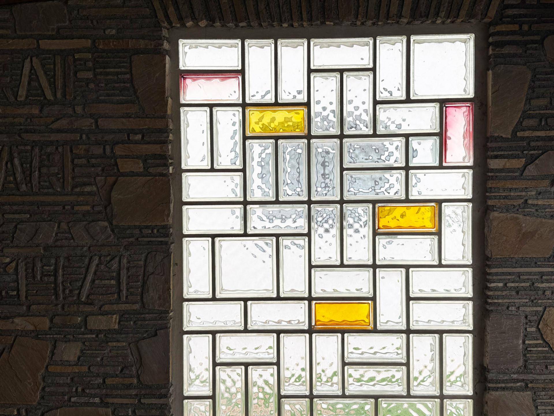 Ein dekoratives Glasbausteinfenster mit farbigen Akzenten in einer rustikalen Steinwand.