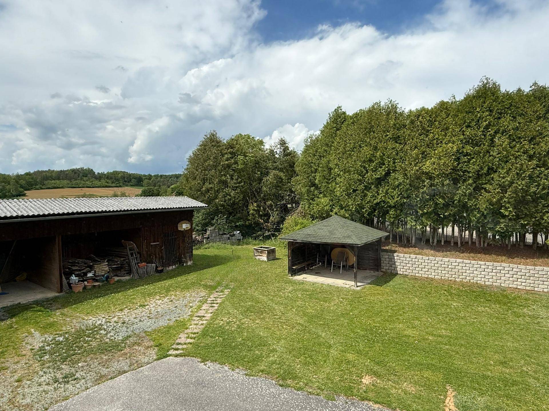 Großer Gartenbereich mit Holzschuppen, Gartenlaube und einer Reihe hoher Bäume.