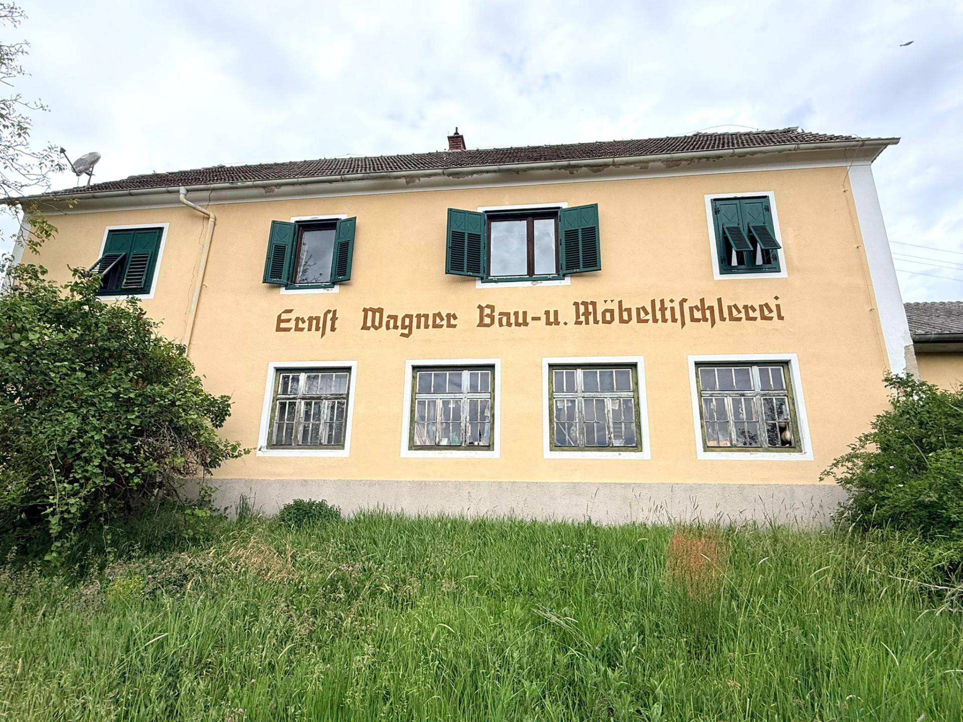 Fassade des Gebäudes mit grünen Fensterläden und Schriftzug einer ehemaligen Tischlerei.