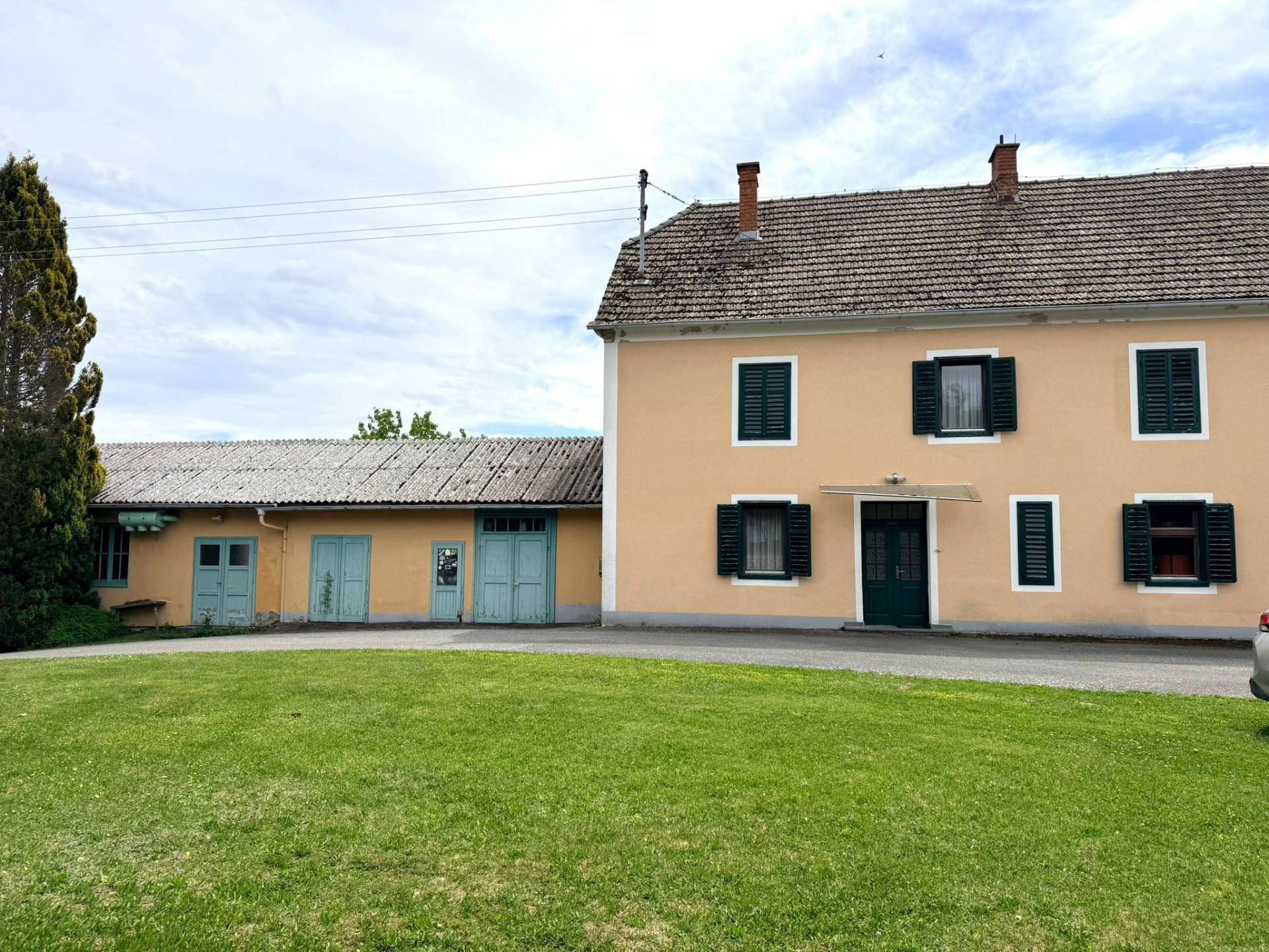 Ansicht des gelben Landhauses mit Nebengebäude und gepflegtem Rasenbereich im Vordergrund.