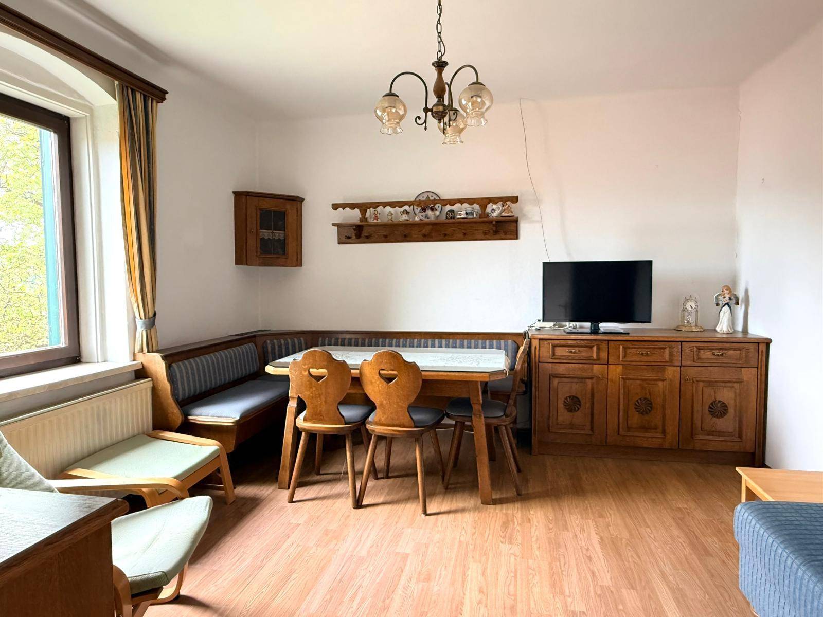 Traditioneller Wohn-Essbereich mit Holztisch, Eckbank und Fernseher auf einem Sideboard.