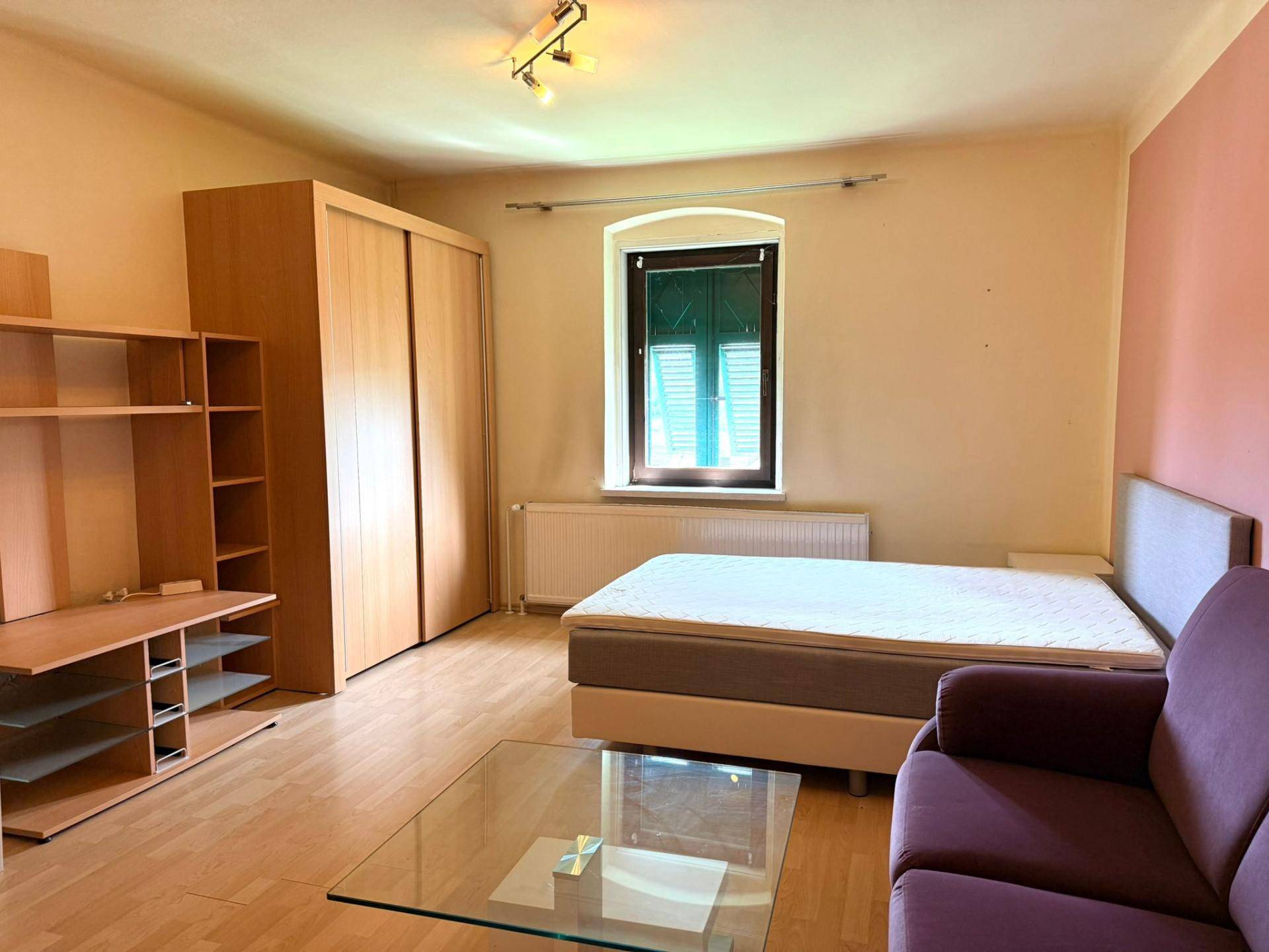 Schlafzimmer mit Bett, Sofa, Kleiderschrank und Fenster mit grünen Fensterläden.