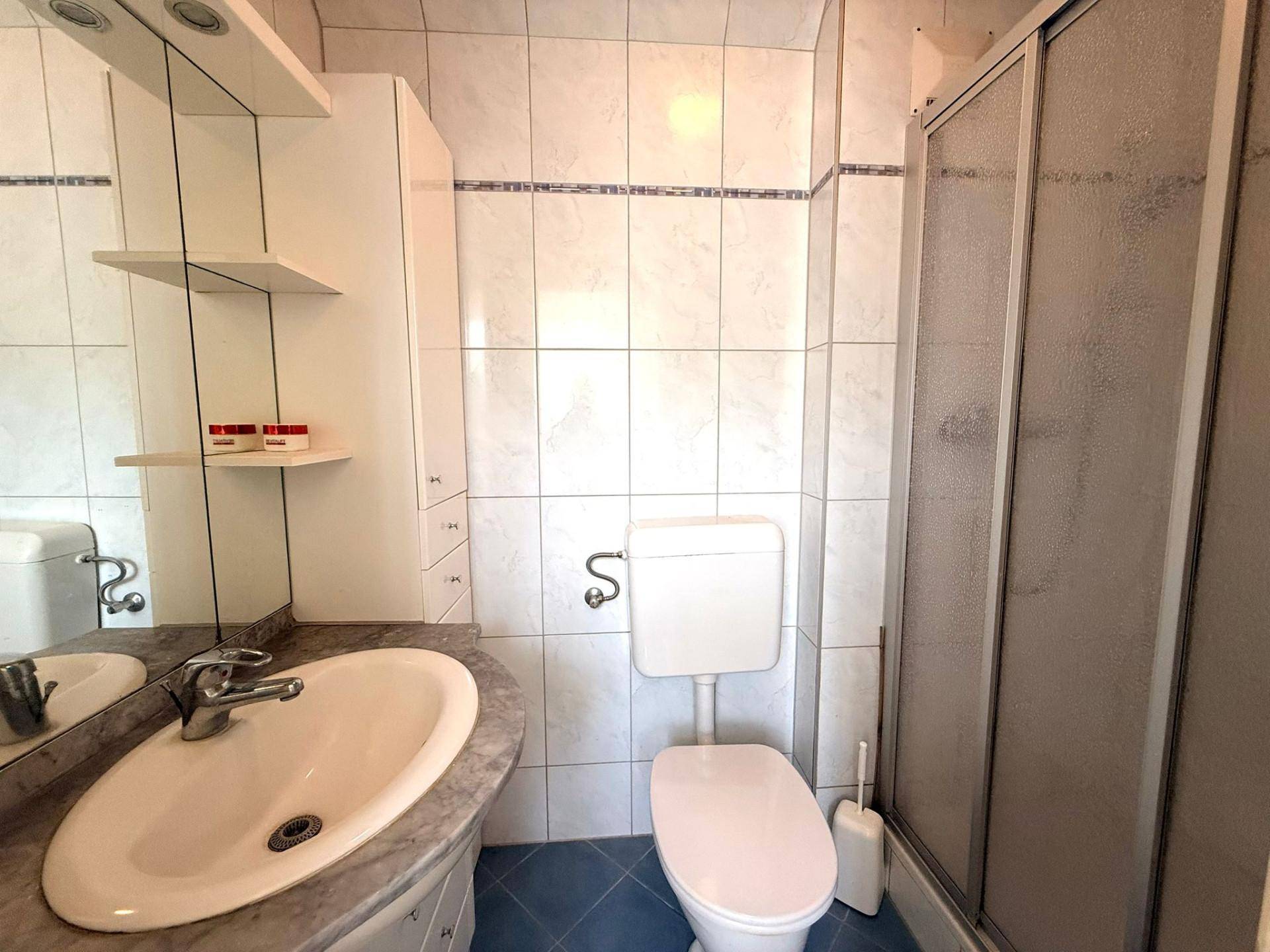 Badezimmer mit Waschbecken, Toilette und Duschkabine, gefliest in Weiß und Blau.