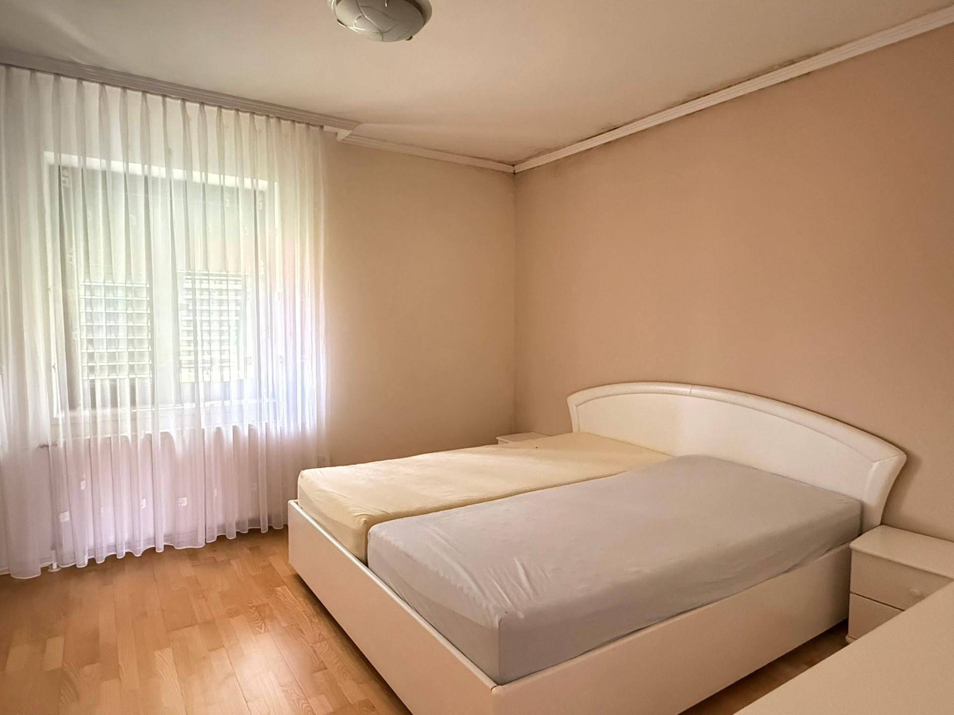 Schlafzimmer mit zwei Einzelbetten, Holzfußboden und hellem Fenster mit Vorhängen.
