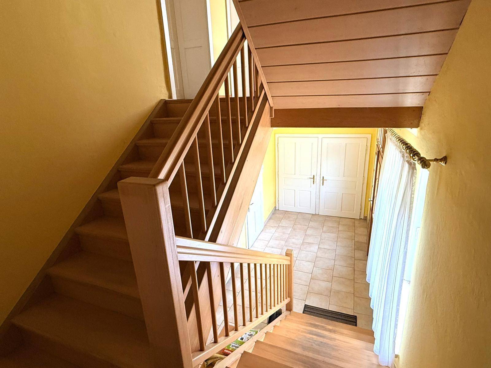 Holztreppe mit Geländer führt in die obere Etage, Fliesenboden im Eingangsbereich.