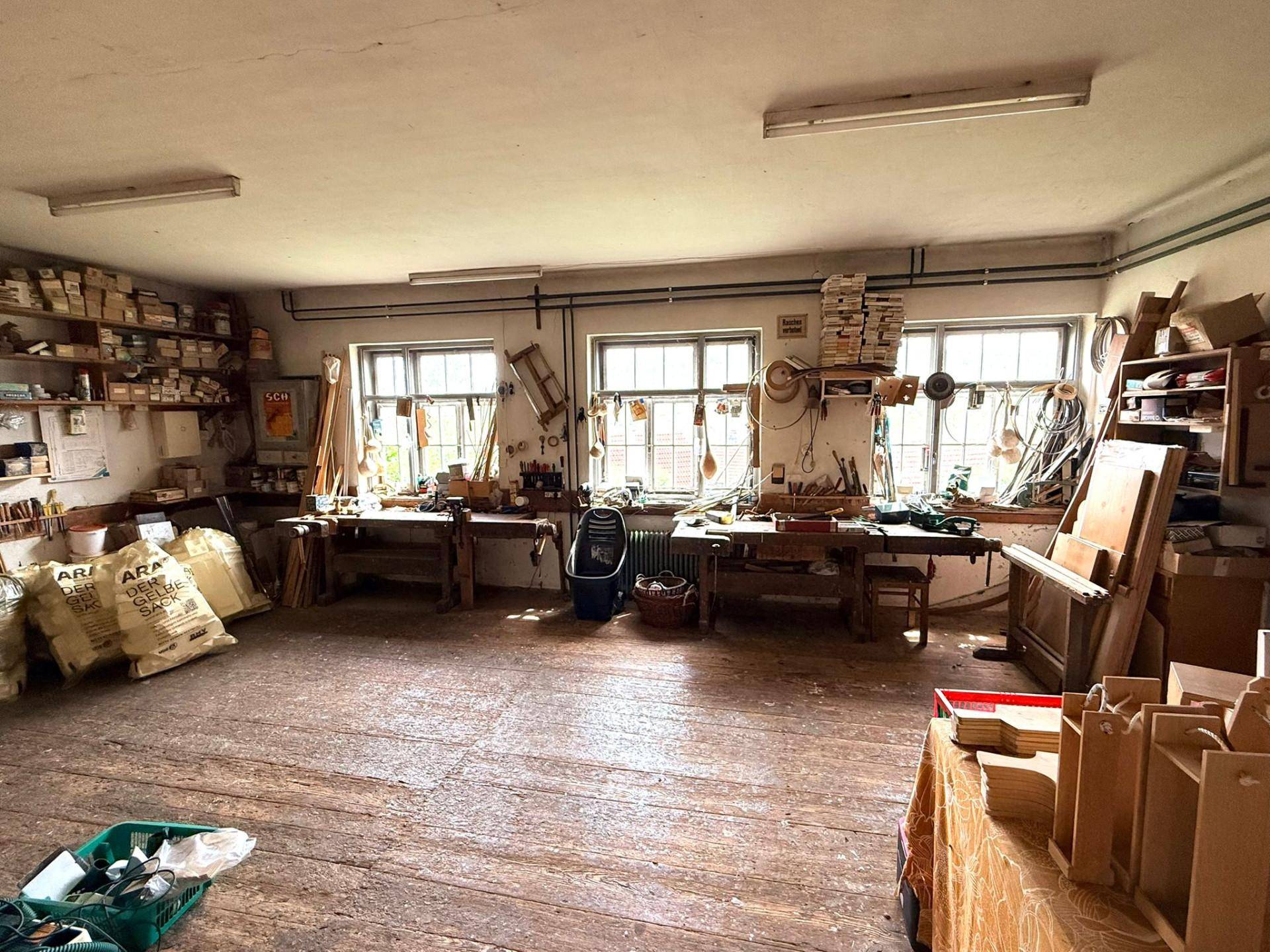 Weitere Ansicht der Werkstatt mit mehreren Werkbänken und Regalen voller Materialien.