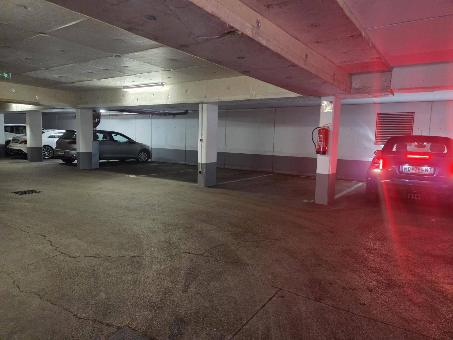 Tiefgarage mit Betonstützen und mehreren geparkten Fahrzeugen, gut beleuchtet.