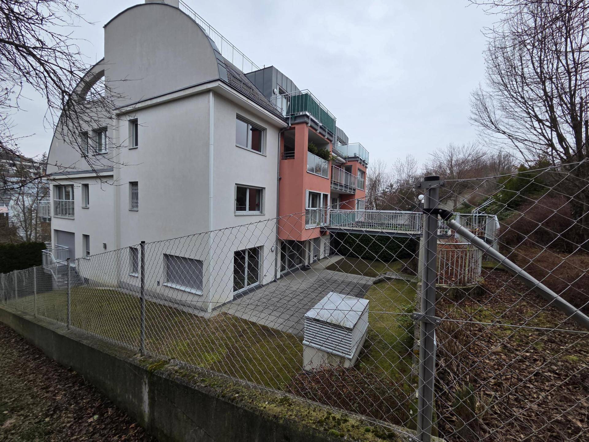 Rückseite des Gebäudes mit mehreren Balkonen, einer kleinen Rasenfläche und umgebender Natur.