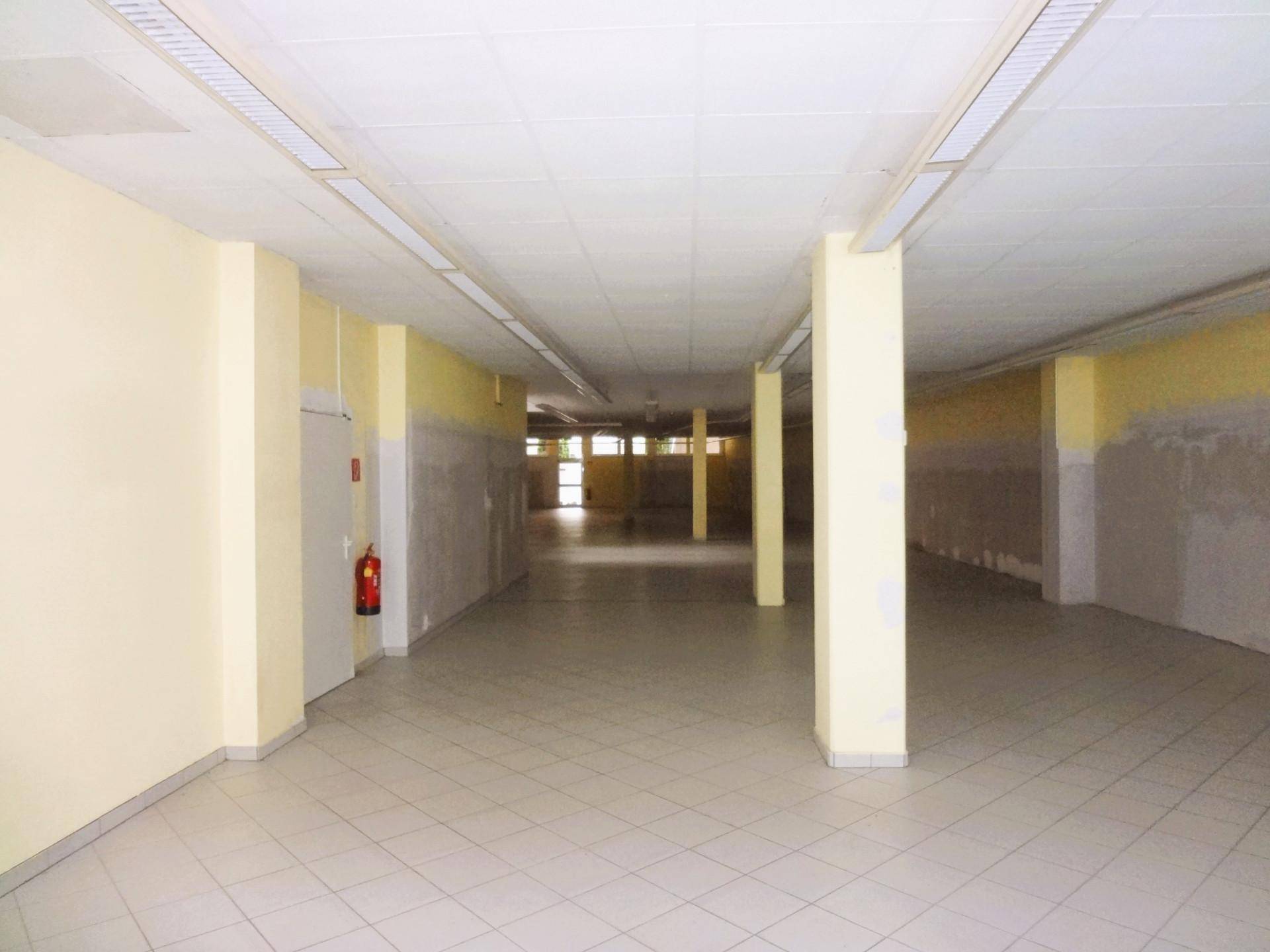 Ein großer, leerer Gewerberaum mit Fliesenboden, Säulen und gelb gestrichenen Wänden.