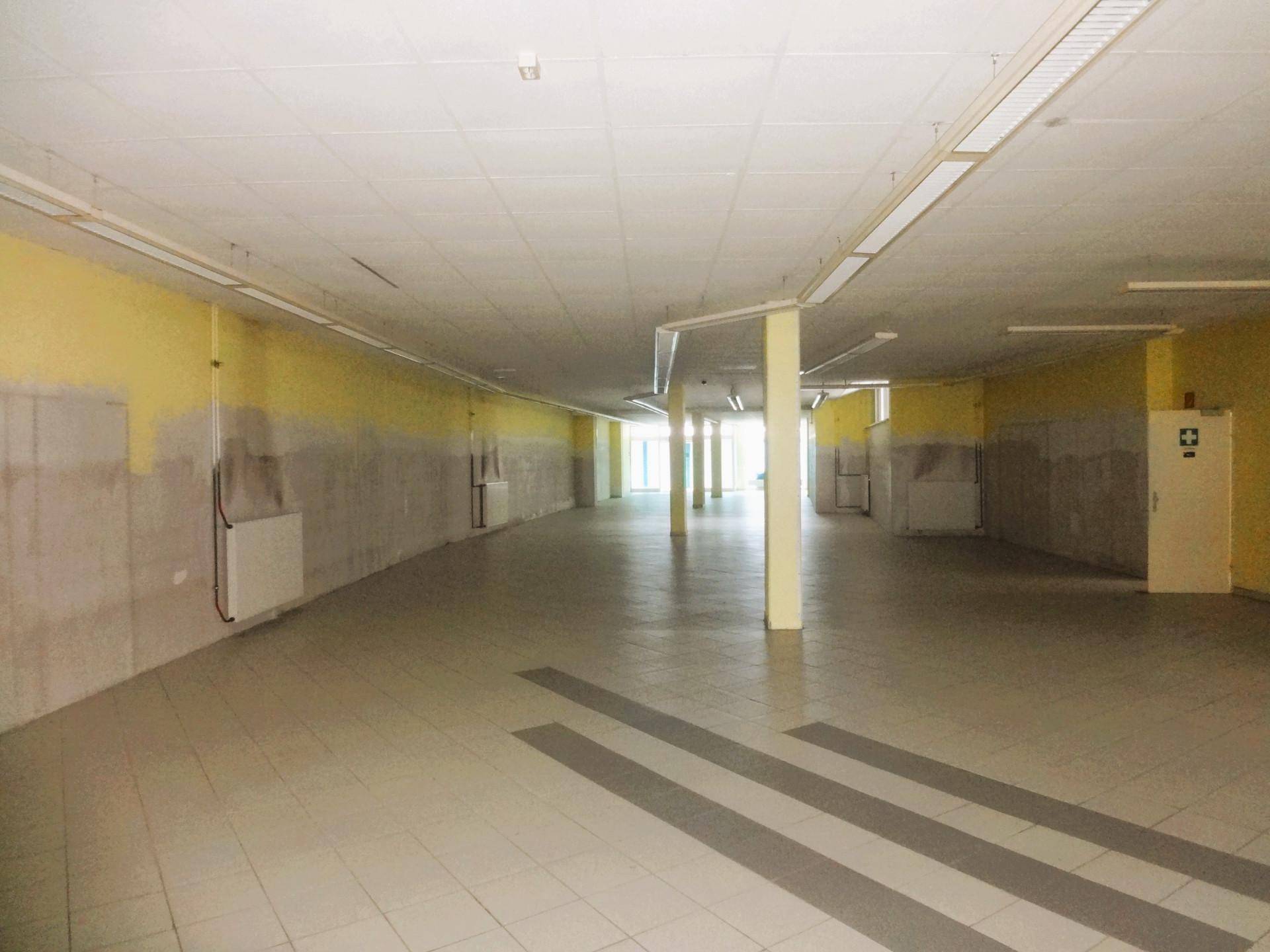 Weitläufiger Gewerberaum mit Fliesenboden, Säulen und einer Mischung aus gestrichenen und rohen Wänden.