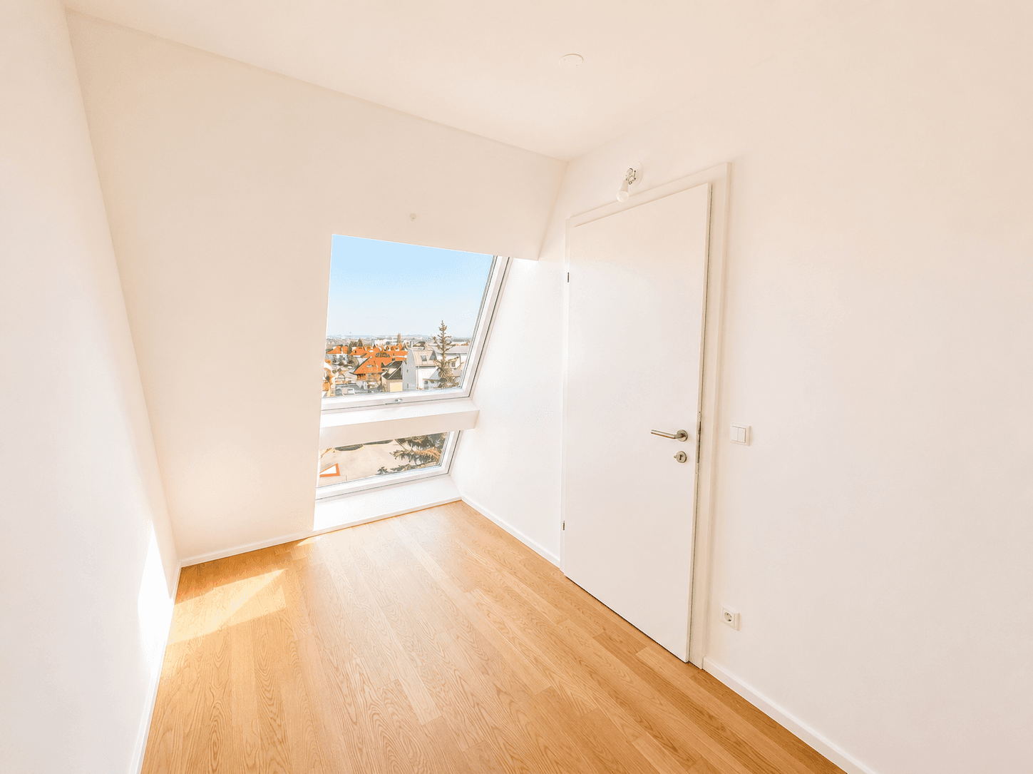 Kleiner, heller Raum mit Holzboden, einer Tür und einem großen Dachfenster.