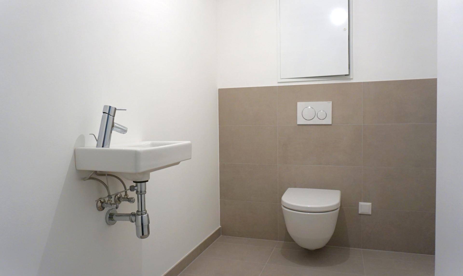 Modernes Gäste-WC mit wandhängender Toilette und kleinem Waschbecken in neutralen Farbtönen.