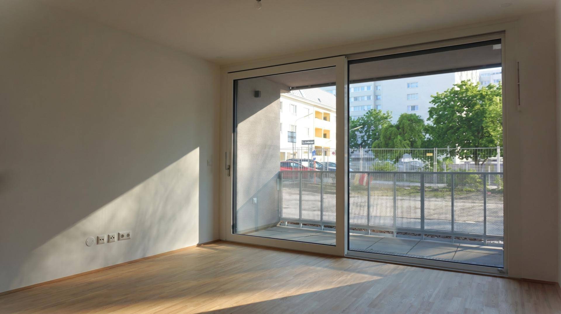 Heller Wohnraum mit Holzboden und großem Schiebefenster, das Zugang zu einem Balkon bietet.