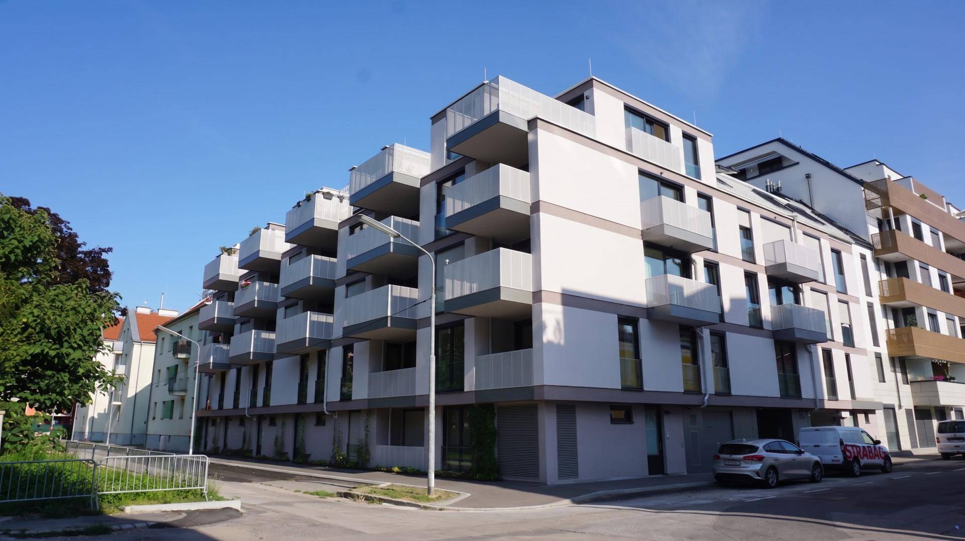 Eckansicht eines modernen Mehrfamilienhauses mit gestaffelten Balkonen und klarem blauem Himmel.