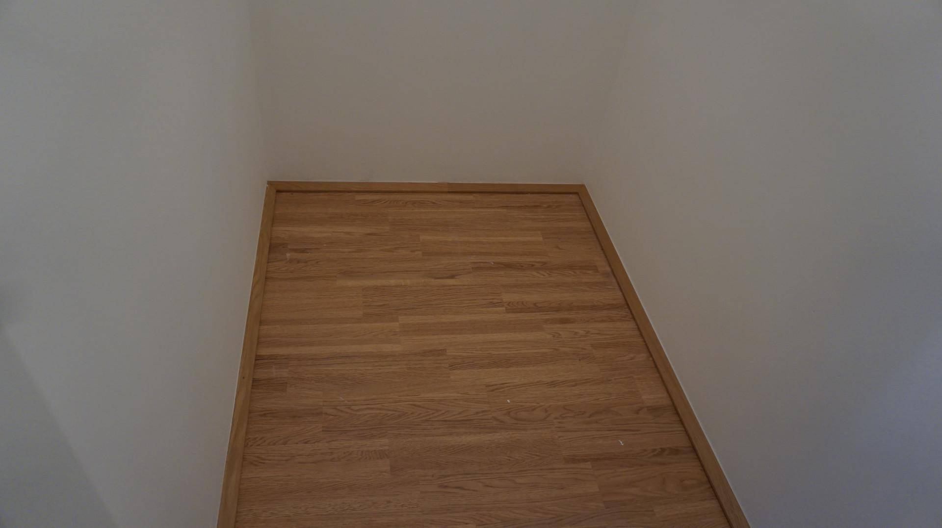Detailaufnahme eines hellen Holzbodens mit weißen Wänden und sauberer Fußleiste in einem Innenraum.