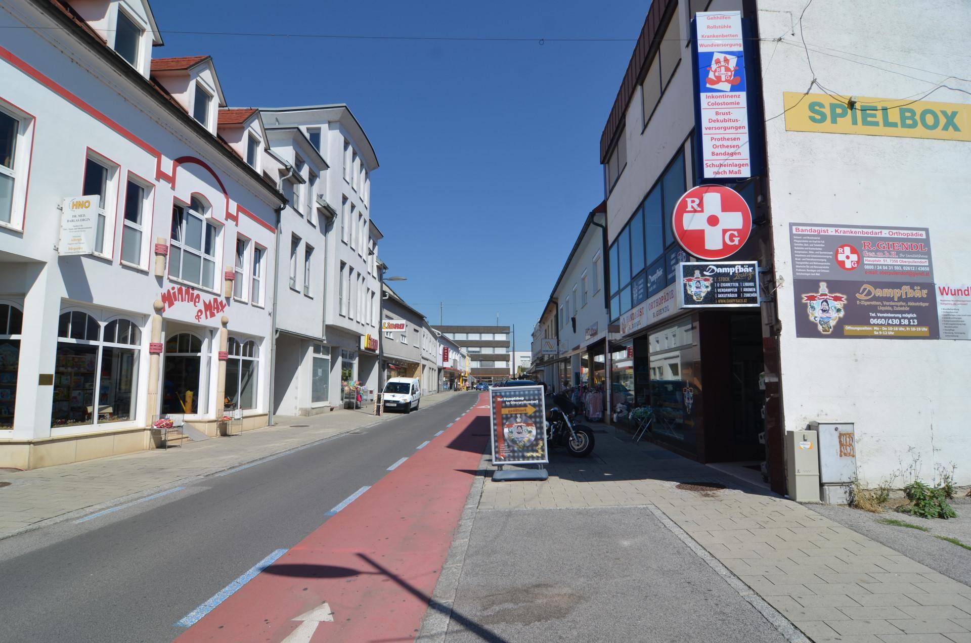 Eine belebte Geschäftsstraße mit verschiedenen Gebäuden und Geschäften unter klarem blauem Himmel.