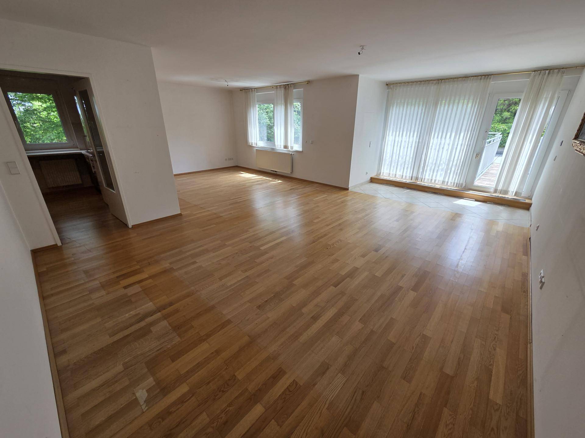 Helles Wohnzimmer mit Parkettboden, weißen Wänden und Zugang zu einem Außenbereich.