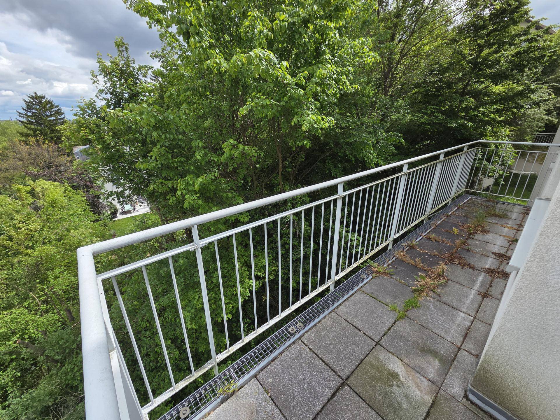 Balkon mit Fliesenboden und Metallgeländer, bietet einen weiten Blick über Bäume.