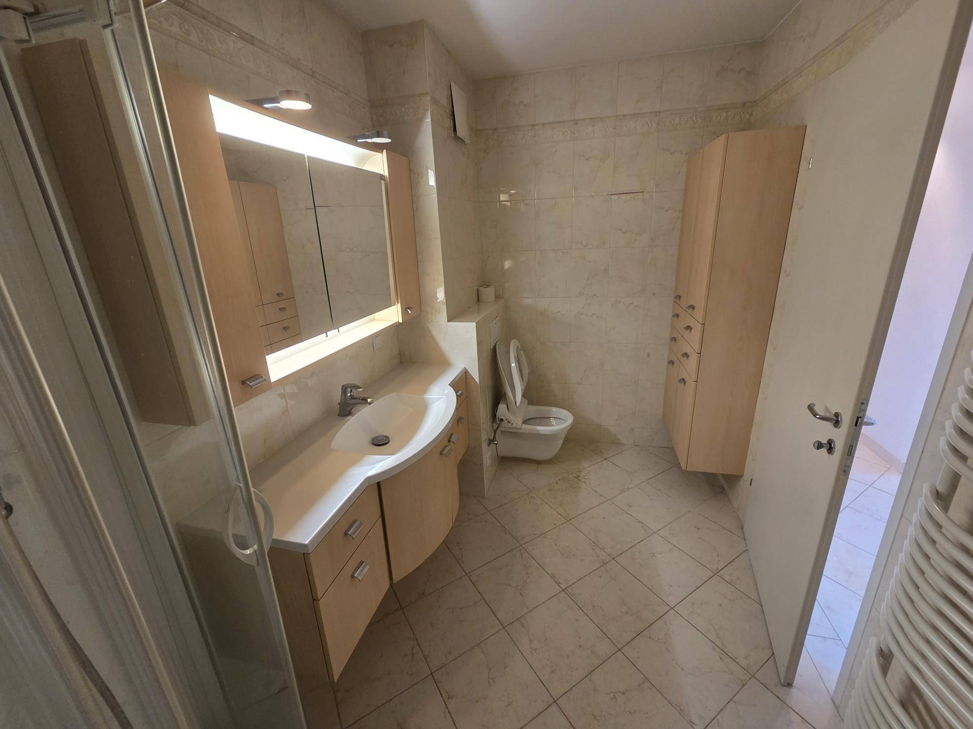 Badezimmer mit hellen Fliesen, Waschtisch mit Spiegelschrank und wandhängendem WC.