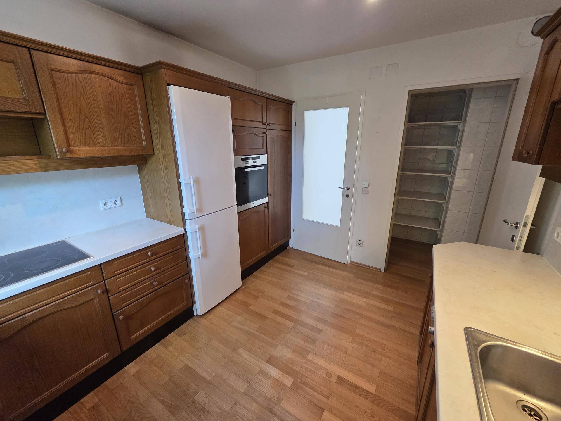 Küche mit Holzschränken, Kühlschrank, Backofen und Zugang zu einem Vorratsraum.