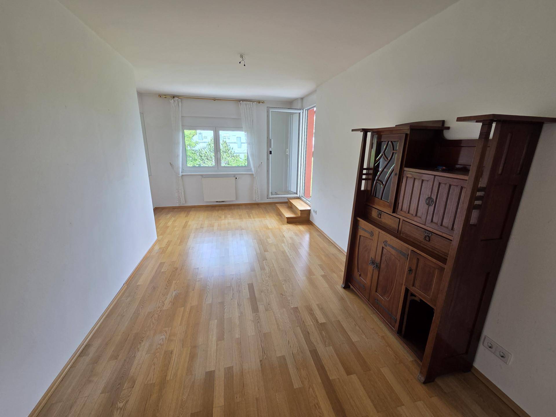 Geräumiges Zimmer mit Parkettboden, Fenstern und einem großen Holzschrank.