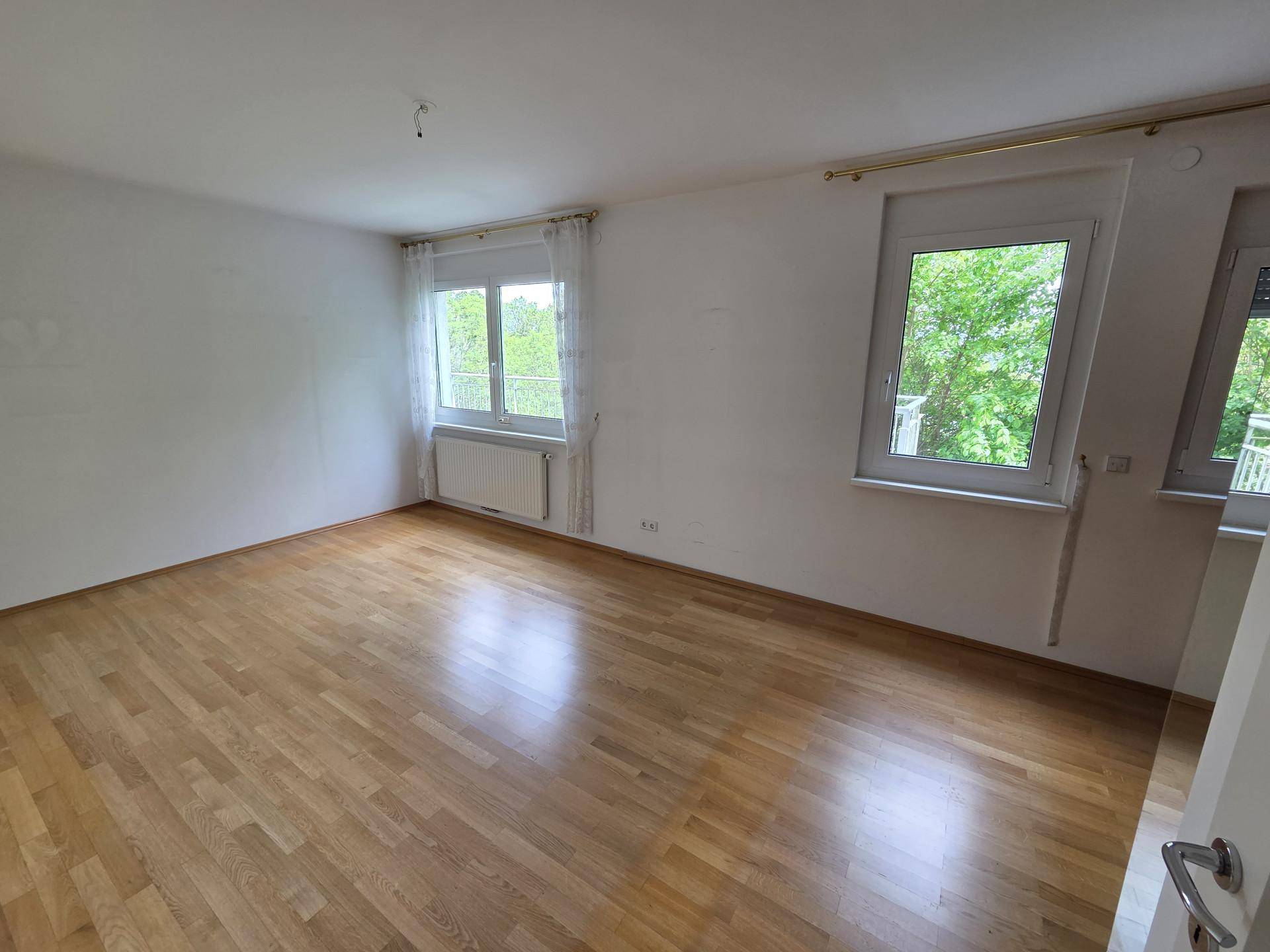 Helles Zimmer mit Parkettboden, zwei Fenstern und einem Heizkörper, bereit zur Einrichtung.
