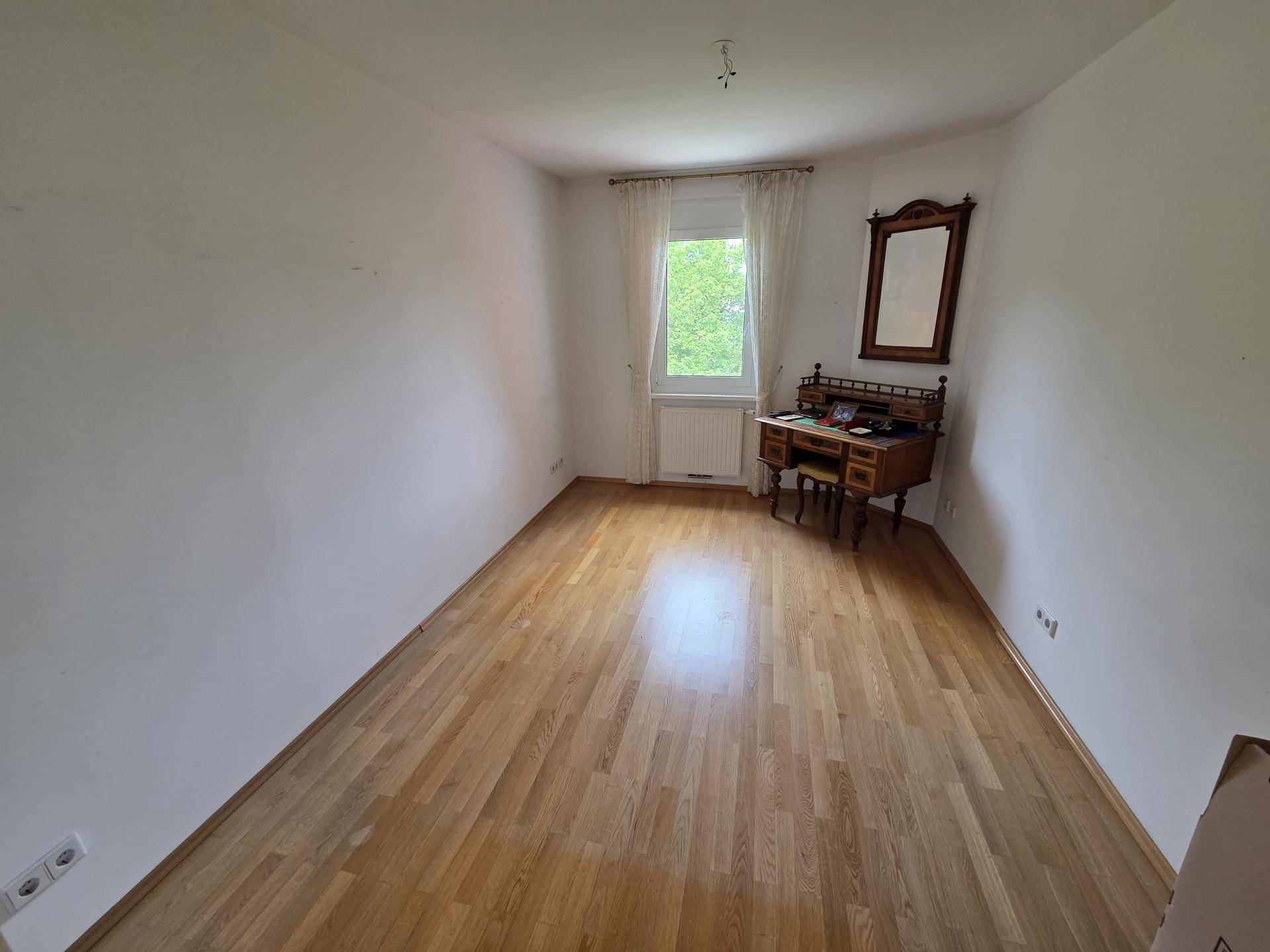 Heller Raum mit Holzfußboden, einem großen Fenster und einem antiken Schreibtisch.