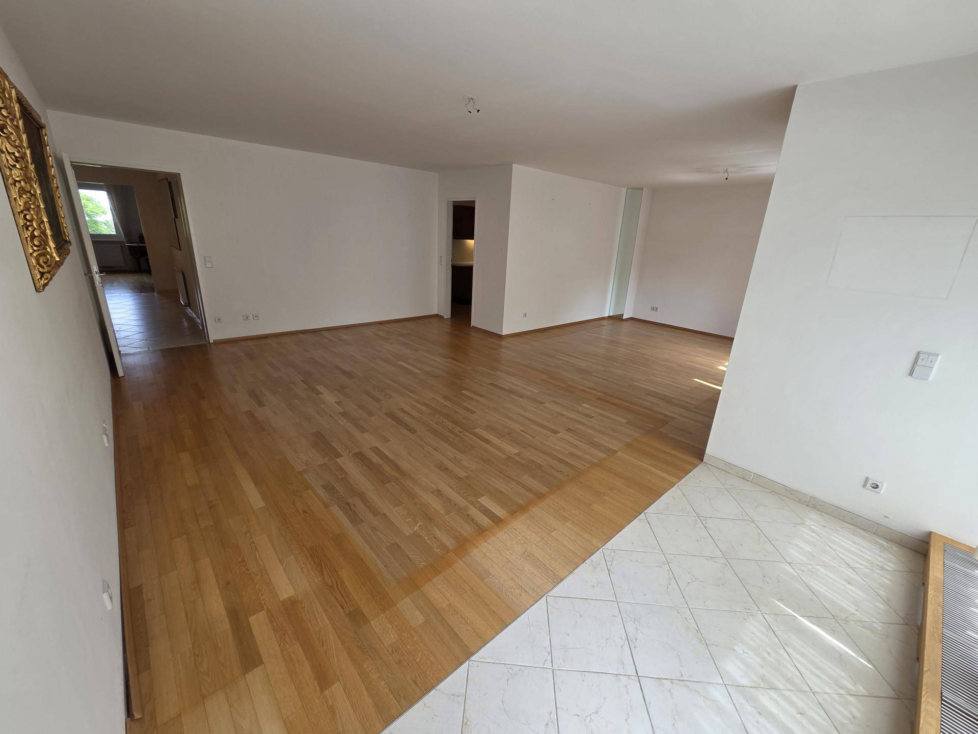 Großes leeres Zimmer mit einer Kombination aus Parkett- und Fliesenboden.